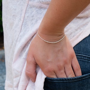 May include: A silver beaded bracelet on a person's wrist. The bracelet is made of small, round beads that are evenly spaced.