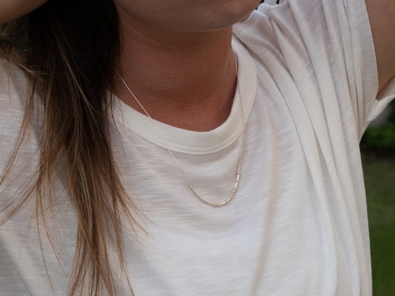 May include: A close-up of a woman wearing a white t-shirt with a silver necklace. The necklace is made of small, round beads.