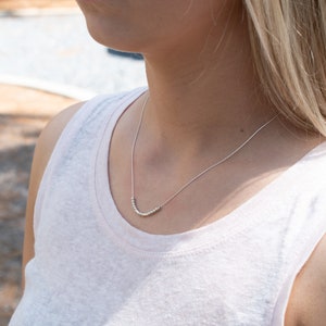 May include: A silver necklace with a curved row of small beads.