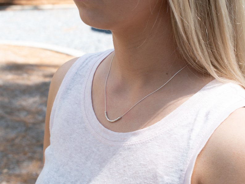 May include: A silver necklace with a curved row of small beads.