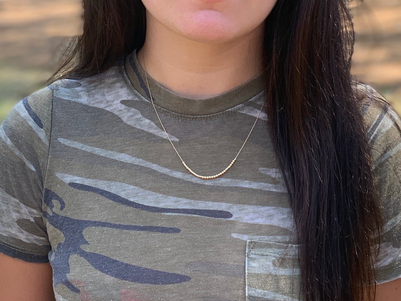 May include: A gold beaded necklace on a person wearing a camouflage shirt.
