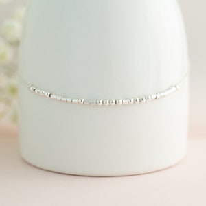 May include: A delicate silver chain anklet with small round and rectangular beads.