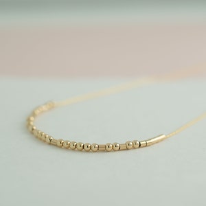 May include: A gold necklace with a delicate chain and a row of small gold beads and bars.