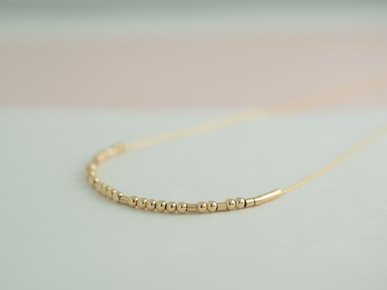 May include: A gold necklace with a delicate chain and a row of small gold beads and bars.