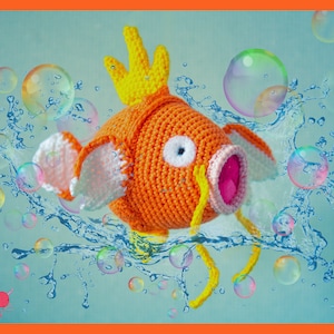 May include: An orange crocheted fish with yellow fins and a yellow crown. The fish has a white and pink mouth and white fins. The background features water splashes and bubbles. The fish is a handmade item.