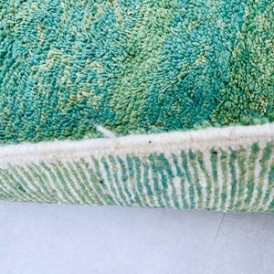K&ouml;nnte beinhalten: Nahaufnahme des Randes eines gr&uuml;n-wei&szlig;en Teppichs. Der Teppich hat einen dicken, flauschigen Flor und einen wei&szlig;en Fransen.