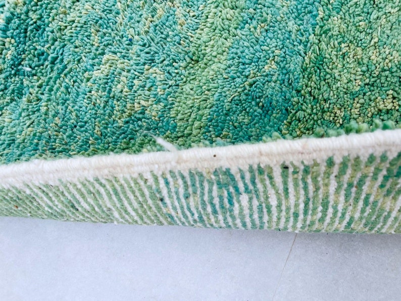 K&ouml;nnte beinhalten: Nahaufnahme des Randes eines gr&uuml;n-wei&szlig;en Teppichs. Der Teppich hat einen dicken, flauschigen Flor und einen wei&szlig;en Fransen.