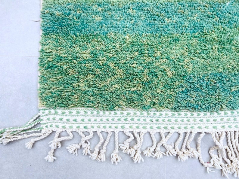 K&ouml;nnte beinhalten: Ein gr&uuml;ner und blauer Shaggy-Teppich mit einem wei&szlig;en Fransenrand. Der Teppich hat einen subtilen Ombre-Effekt, der von einem dunkleren Gr&uuml;n zu einem helleren Blau &uuml;bergeht.