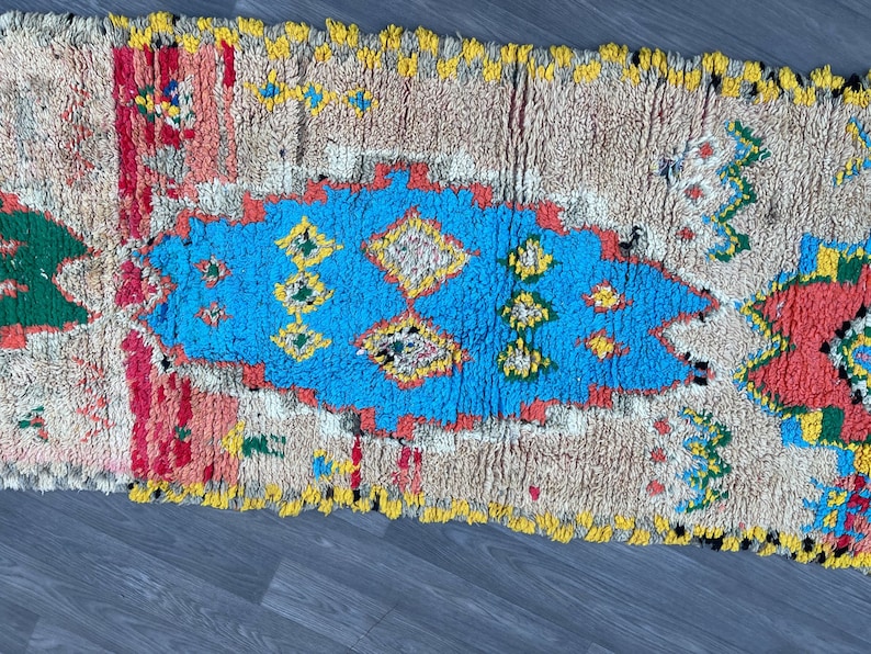 Puede incluir: Una alfombra marroqu&iacute; colorida con un patr&oacute;n geom&eacute;trico azul, amarillo, rojo y verde. La alfombra tiene un fondo blanco y est&aacute; hecha de lana.