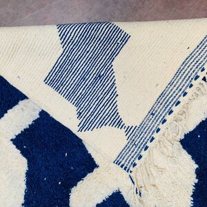 May include: A white and blue woven rug with a geometric pattern. The rug has a fringe border.