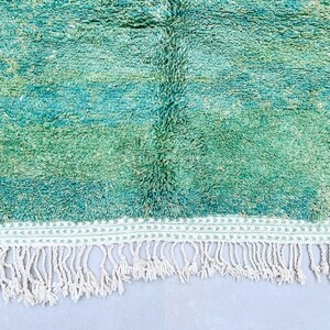 K&ouml;nnte beinhalten: Ein handgewebter Teppich in Teal- und Gr&uuml;nt&ouml;nen mit einem wei&szlig;en Fransenrand. Der Teppich hat einen subtilen Ombre-Effekt, der von einem dunkleren Teal zu einem helleren Gr&uuml;n &uuml;bergeht.