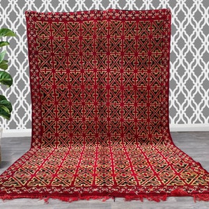 K&ouml;nnte beinhalten: Ein roter und schwarzer geometrisch gemusterter Teppich mit Fransenbord&uuml;re. Der Teppich hat ein traditionelles marokkanisches Design.