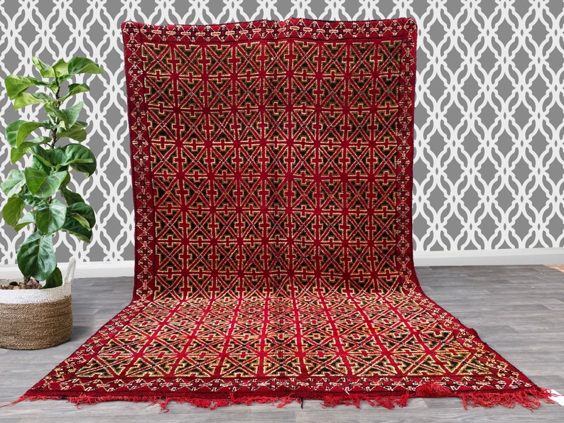 K&ouml;nnte beinhalten: Ein roter und schwarzer geometrisch gemusterter Teppich mit Fransenbord&uuml;re. Der Teppich hat ein traditionelles marokkanisches Design.