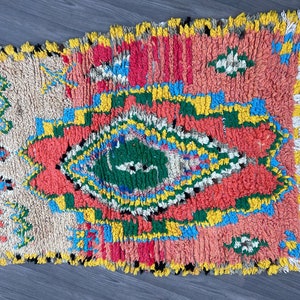 Puede incluir: Una alfombra marroqu&iacute; colorida con un patr&oacute;n geom&eacute;trico en tonos de rojo, azul, verde, amarillo y blanco. La alfombra tiene un borde de flecos y est&aacute; hecha de lana.
