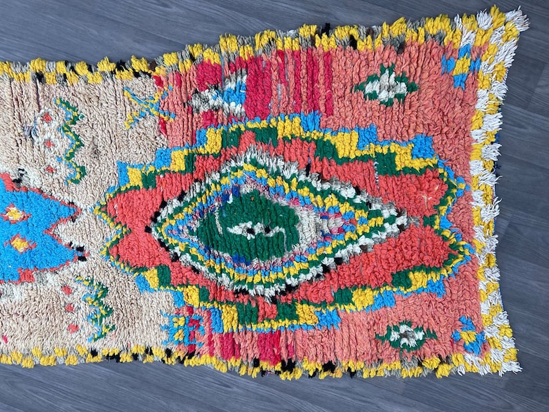 Puede incluir: Una alfombra marroqu&iacute; colorida con un patr&oacute;n geom&eacute;trico en tonos de rojo, azul, verde, amarillo y blanco. La alfombra tiene un borde de flecos y est&aacute; hecha de lana.
