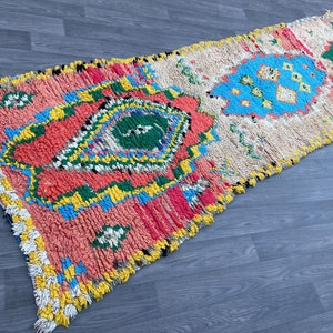 Puede incluir: Una alfombra marroqu&iacute; colorida con un patr&oacute;n geom&eacute;trico en tonos de rosa, azul, verde y amarillo. La alfombra tiene un borde con flecos y est&aacute; hecha de lana.