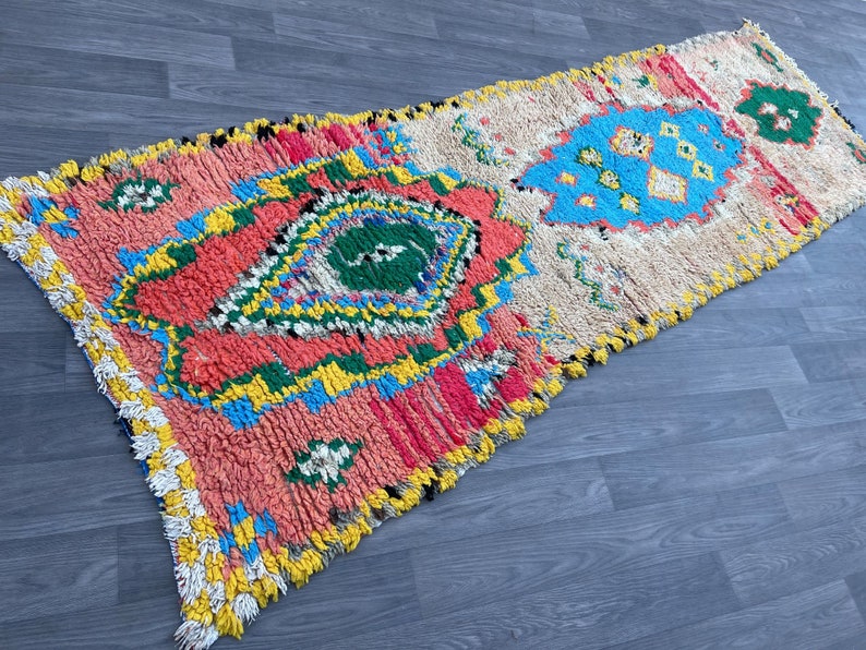 Puede incluir: Una alfombra marroqu&iacute; colorida con un patr&oacute;n geom&eacute;trico en tonos de rosa, azul, verde y amarillo. La alfombra tiene un borde con flecos y est&aacute; hecha de lana.