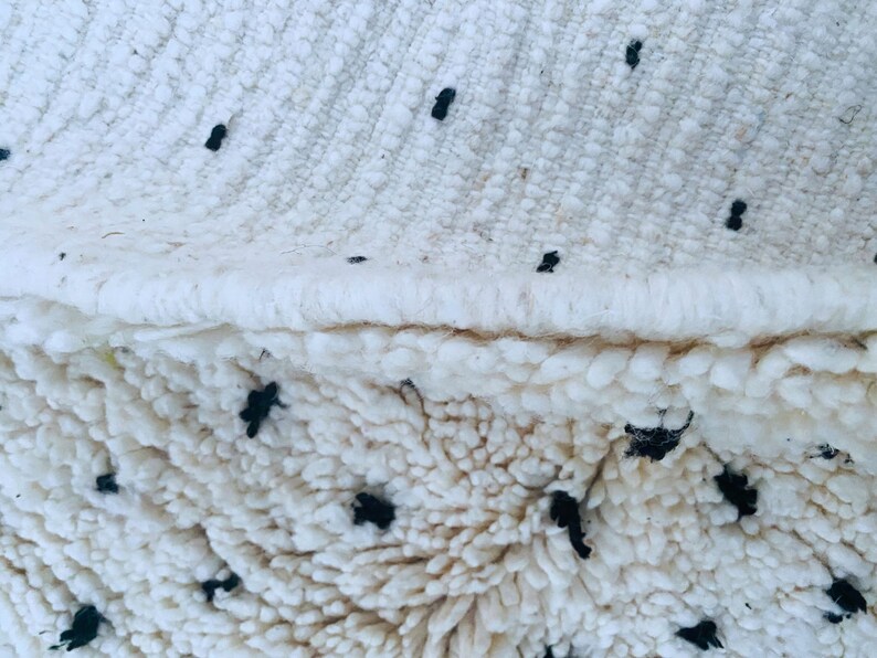 May include: Close-up of a white fluffy rug with black dots. The rug has a woven edge.
