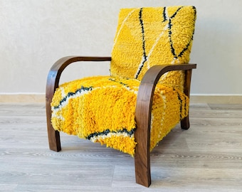 May include: A yellow armchair with a wooden frame and a thick, patterned fabric upholstery. The fabric has a geometric design with black and white lines.