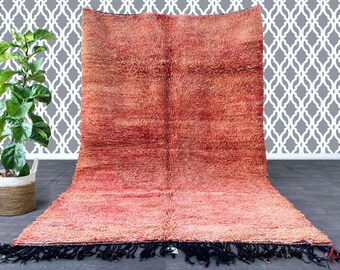 May include: A large, rectangular rug with a shaggy texture. The rug features a gradient of colors, transitioning from a deep red at the top to a lighter pink at the bottom. The rug has a dark blue fringe along the bottom edge. The rug is displayed on a gray surface.