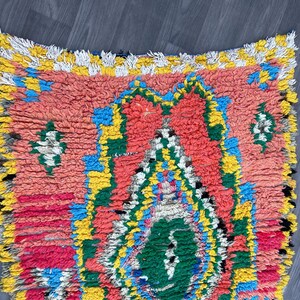 Puede incluir: Una alfombra marroqu&iacute; colorida con un patr&oacute;n geom&eacute;trico en tonos rojos, amarillos, azules y verdes. La alfombra tiene un borde con flecos y est&aacute; hecha de lana.