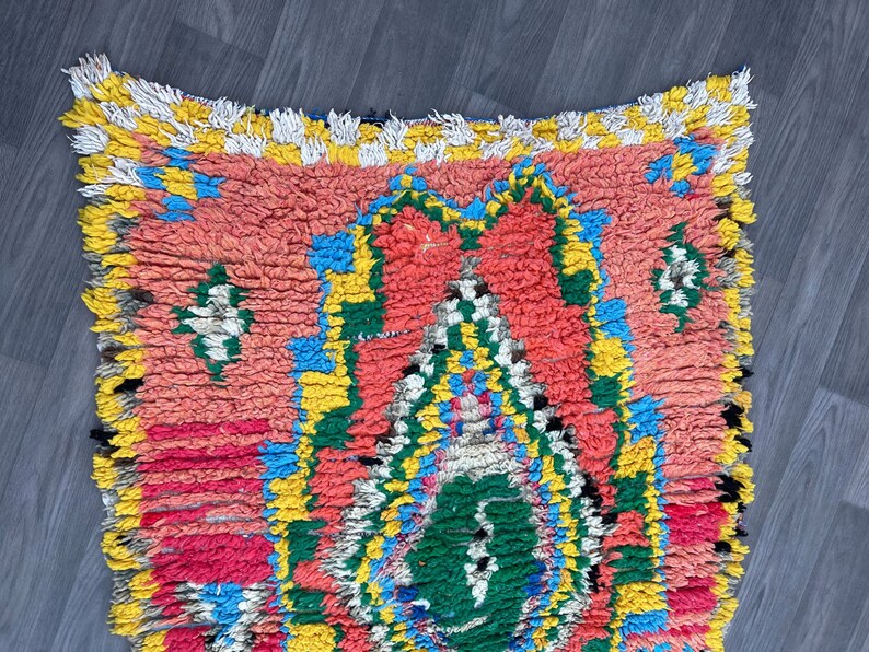 Puede incluir: Una alfombra marroqu&iacute; colorida con un patr&oacute;n geom&eacute;trico en tonos rojos, amarillos, azules y verdes. La alfombra tiene un borde con flecos y est&aacute; hecha de lana.
