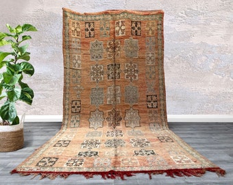 May include: A vintage Moroccan rug with a geometric pattern in shades of brown, red, and blue. The rug has a fringe border and is made of wool.