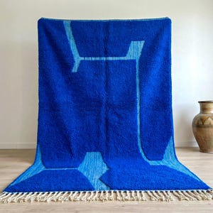 Handmade blue Beni Ourain Moroccan rug displayed vertically with abstract Berber pattern and wool fringe