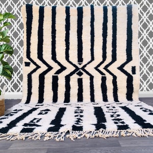 Puede incluir: Alfombra marroquí en blanco y negro con un patrón geométrico. La alfombra tiene un borde de flecos y está hecha de lana.