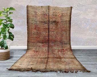 May include: A vintage Moroccan rug with a geometric pattern in shades of brown, red, and beige. The rug has a fringe border and is woven with a distressed look.