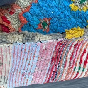 Puede incluir: Primer plano de una alfombra marroqu&iacute; colorida con una variedad de texturas y patrones. La alfombra est&aacute; hecha de lana y tiene un borde de flecos. La alfombra est&aacute; en tonos de azul, rojo, amarillo, blanco y gris.