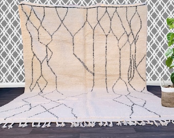 May include: A white Moroccan rug with a black geometric pattern. The rug has a fringe border and is made of wool.