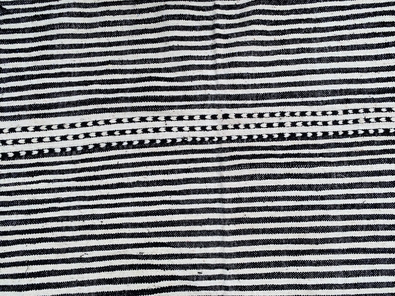 Wool Moroccan rug handwoven with alternating black and white stripes running vertically (see photos). Authentic Berber craftsmanship is reflected in its balanced design and fringed finish. This durable carpet complements Scandinavian-inspired interiors, bohemian spaces, or modern homes, providing cultural authenticity, texture, and timeless Moroccan artistry to any room.
