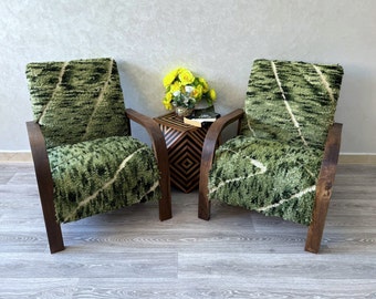 May include: Two green patterned armchairs with dark wood frames, facing each other, with a small wooden table with a geometric pattern in between.