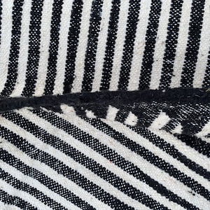 Moroccan striped rug handwoven in soft wool, alternating bold black and white lines across its surface (see photos). This authentic Berber carpet is both stylish and durable, with fringed edges for cultural charm. Ideal for modern apartments, bohemian spaces, or minimalist interiors, it offers heritage, elegance, and warmth in one timeless design.