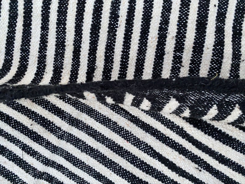 Moroccan striped rug handwoven in soft wool, alternating bold black and white lines across its surface (see photos). This authentic Berber carpet is both stylish and durable, with fringed edges for cultural charm. Ideal for modern apartments, bohemian spaces, or minimalist interiors, it offers heritage, elegance, and warmth in one timeless design.