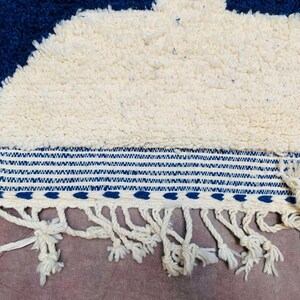 May include: A white and blue rug with a fringe border. The rug features a geometric pattern and is made from a soft, fluffy material.