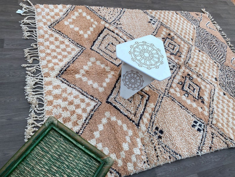 May include: A beige and cream geometric patterned rug with a white, three-legged table. The rug features diamond and checkered patterns with black accents. A green tray is in the foreground.