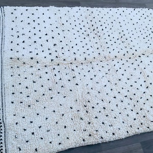May include: A white rug with black dots and fringe on all sides. The rug has a textured, fluffy surface.