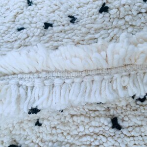 May include: Close-up of a white rug with a fringe border and black dots throughout the design.