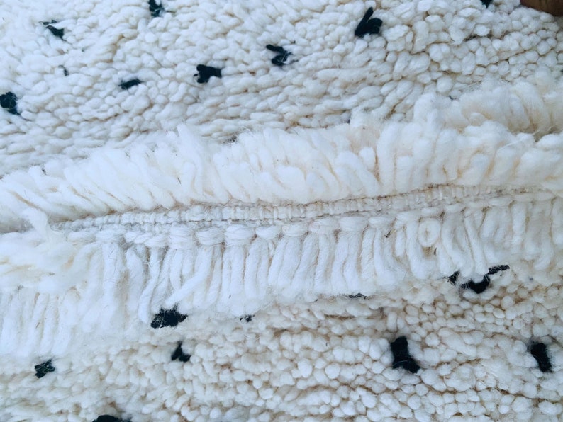 May include: Close-up of a white rug with a fringe border and black dots throughout the design.