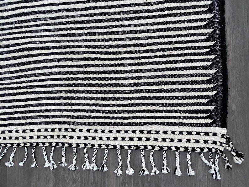 Authentic Moroccan wool rug in a striped pattern, alternating black and white bands that create a bold linear effect (see photos). Finished with fringes, this handmade Berber carpet combines cultural craftsmanship with modern minimalist appeal. A versatile piece that suits bohemian, eclectic, or Scandinavian-inspired homes, offering both comfort and timeless Moroccan artistry.