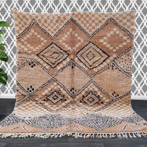 May include: A beige and brown geometric patterned rug with a diamond design. The rug has a textured, plush appearance with a fringe along the bottom edge. The design includes black and white accents.