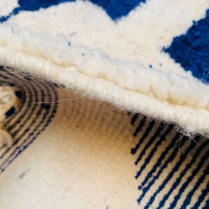May include: Close-up of a white and blue rug with a fringed edge. The rug has a geometric pattern with stripes and circles.