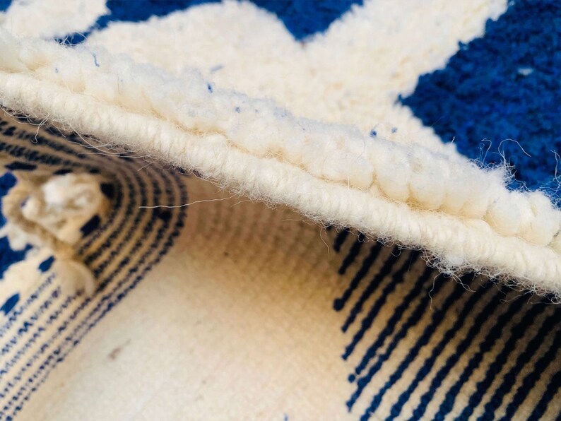 May include: Close-up of a white and blue rug with a fringed edge. The rug has a geometric pattern with stripes and circles.
