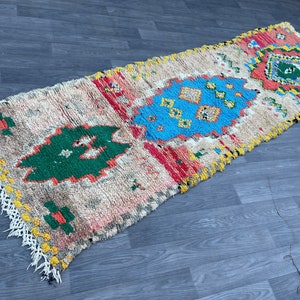 Puede incluir: Una alfombra rectangular larga con fondo crema y patrones geom&eacute;tricos coloridos. La alfombra tiene flecos en ambos extremos y presenta tonos de rojo, azul, verde y amarillo.