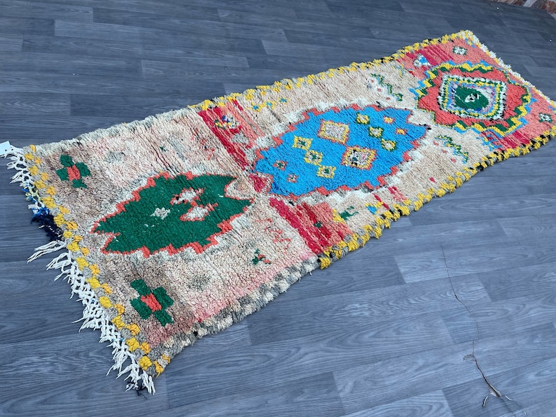 Puede incluir: Una alfombra rectangular larga con fondo crema y patrones geom&eacute;tricos coloridos. La alfombra tiene flecos en ambos extremos y presenta tonos de rojo, azul, verde y amarillo.