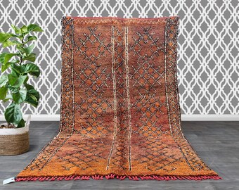 May include: A long, rectangular, orange and brown Moroccan rug with a geometric pattern. The rug has a fringe border.