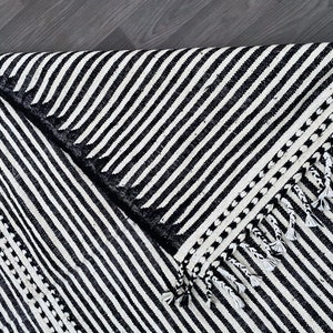 Authentic striped Moroccan rug crafted in ivory and black wool (see photos). Its handwoven linear design highlights Berber craftsmanship with a minimalist twist. Fringes complete the artisanal look, making this rug ideal for boho-chic interiors, Scandinavian homes, or modern spaces seeking cultural depth, comfort, and timeless Moroccan style.