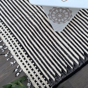 Handwoven Moroccan rug crafted from wool, designed with sleek black and white stripes in a timeless pattern (see photos). This Berber carpet embodies minimalist elegance while preserving traditional craftsmanship. Soft, durable, and fringed, it’s a versatile statement piece for boho living rooms, modern lofts, or cozy bedrooms, adding warmth and Moroccan character.
